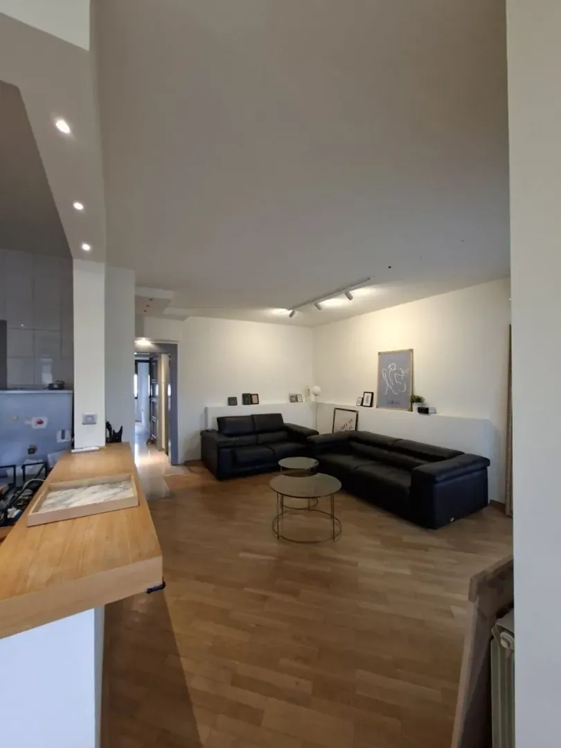 Living room with black leather sofas and wooden flooring.