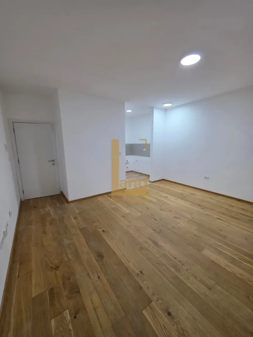 Prazna soba sa drvenim podom i bijelim zidovima.