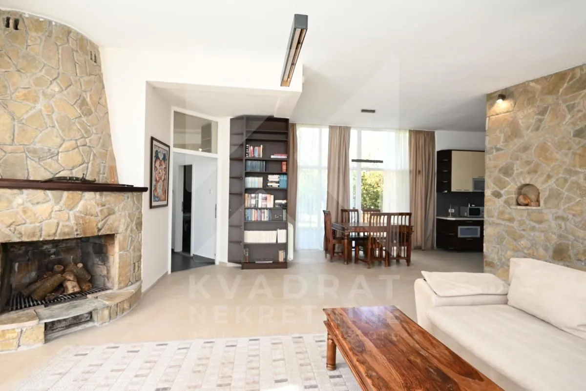 Spacious living room with a stone-clad fireplace and a dining area in the background.