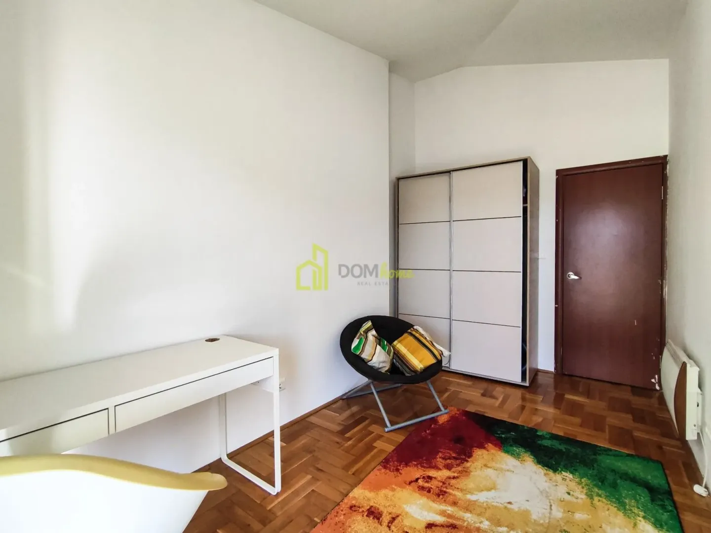 Furnished bedroom with a desk, wardrobe, and colourful rug.