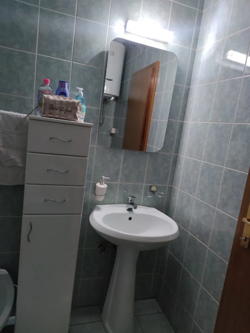 Jednostavno kupatilo sa plavim pločicama, lavaboom i bijelim vertikalnim ormarićem.