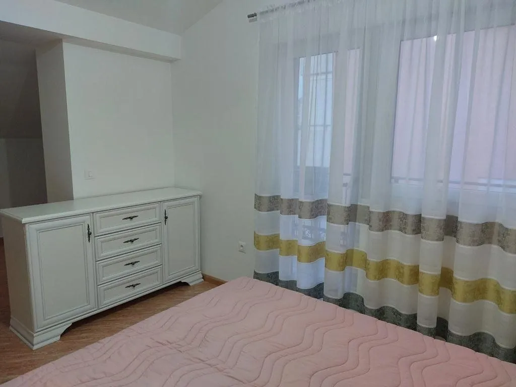 Bedroom with a bed, chest of drawers, and a window with curtains.