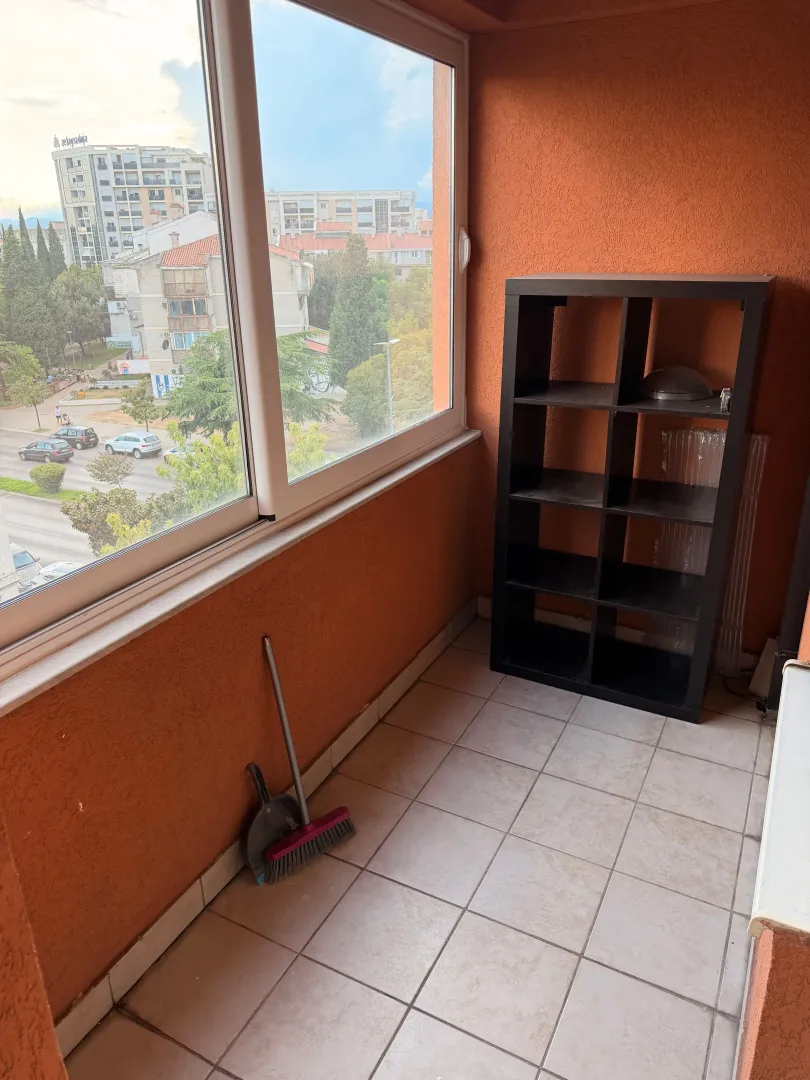 Enclosed balcony with a shelving unit and city view.