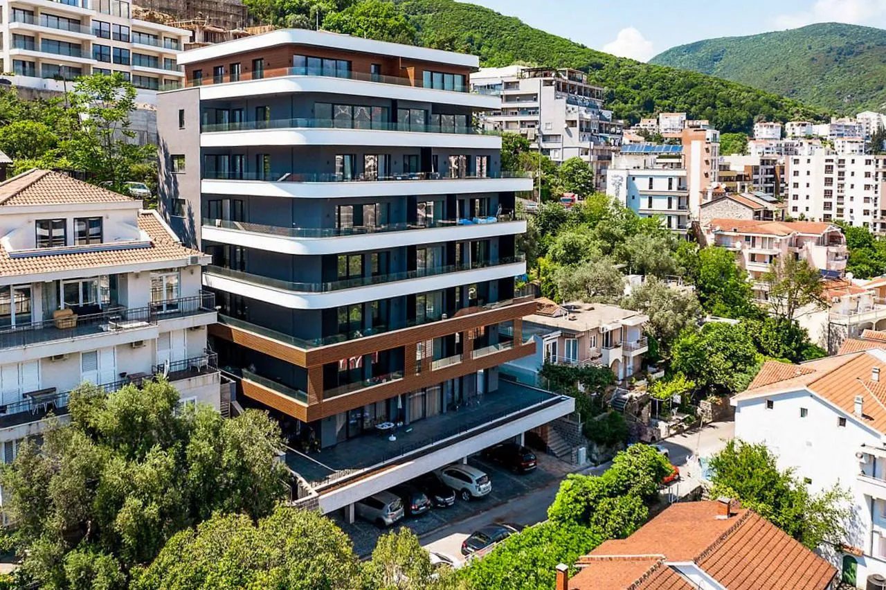 Pogled iz ptičje perspektive na modernu stambenu zgradu sa terasama i parkingom u okruženju.