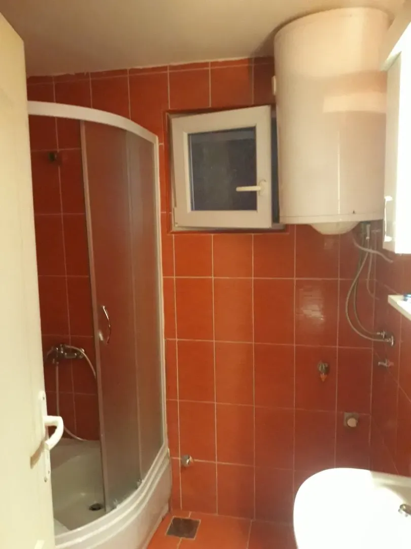 Kupatilo sa narandžastim pločicama, tuš kabinom i bojlerom.