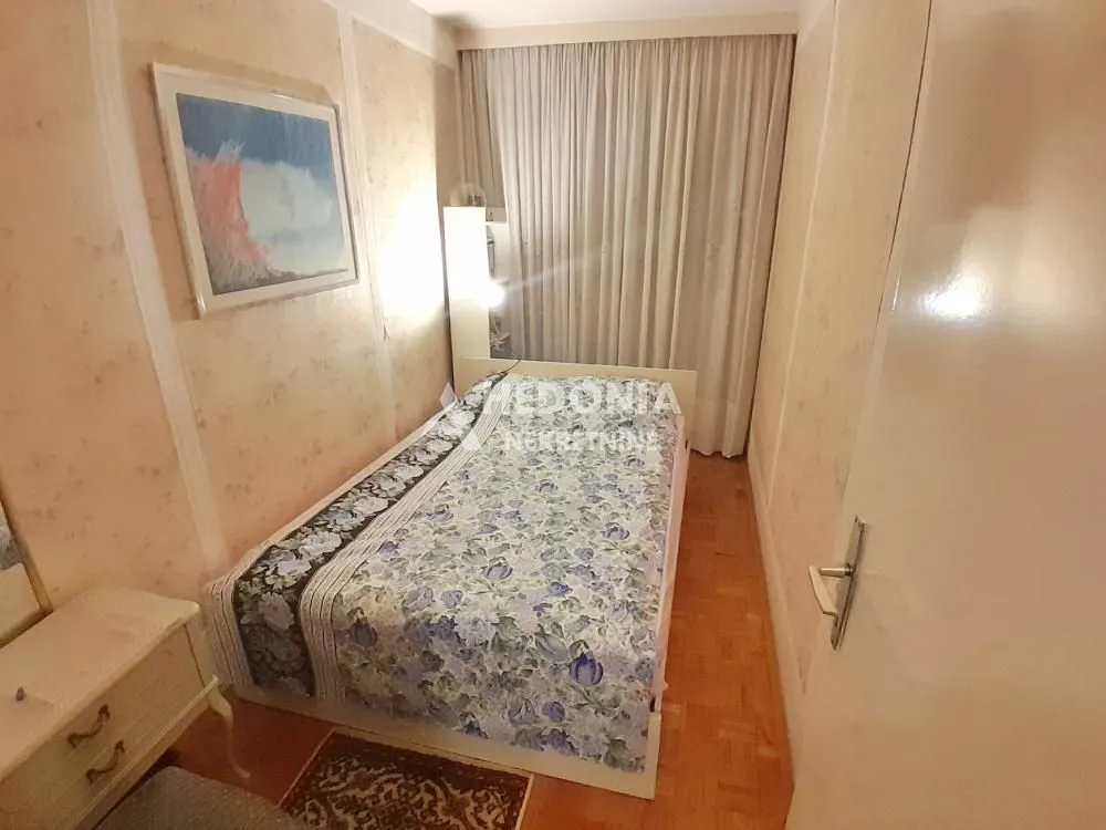 Manja spavaća soba sa krevetom, noćnim stočićem i tapetama na zidovima.