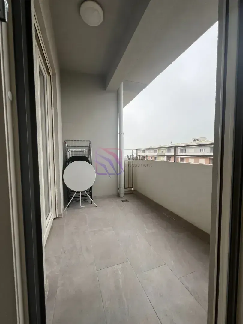 Nakatkriveni balkon sa popločanim podom i odloženim nameštajem.
