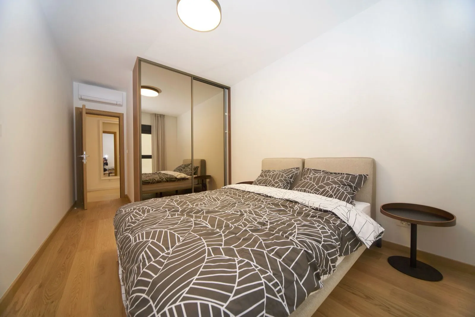Bedroom with a double bed, a large mirrored wardrobe, and hardwood flooring.