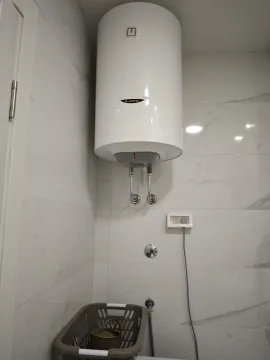 Bijeli električni bojler montiran na popločanom zidu kupatila. - image 14
