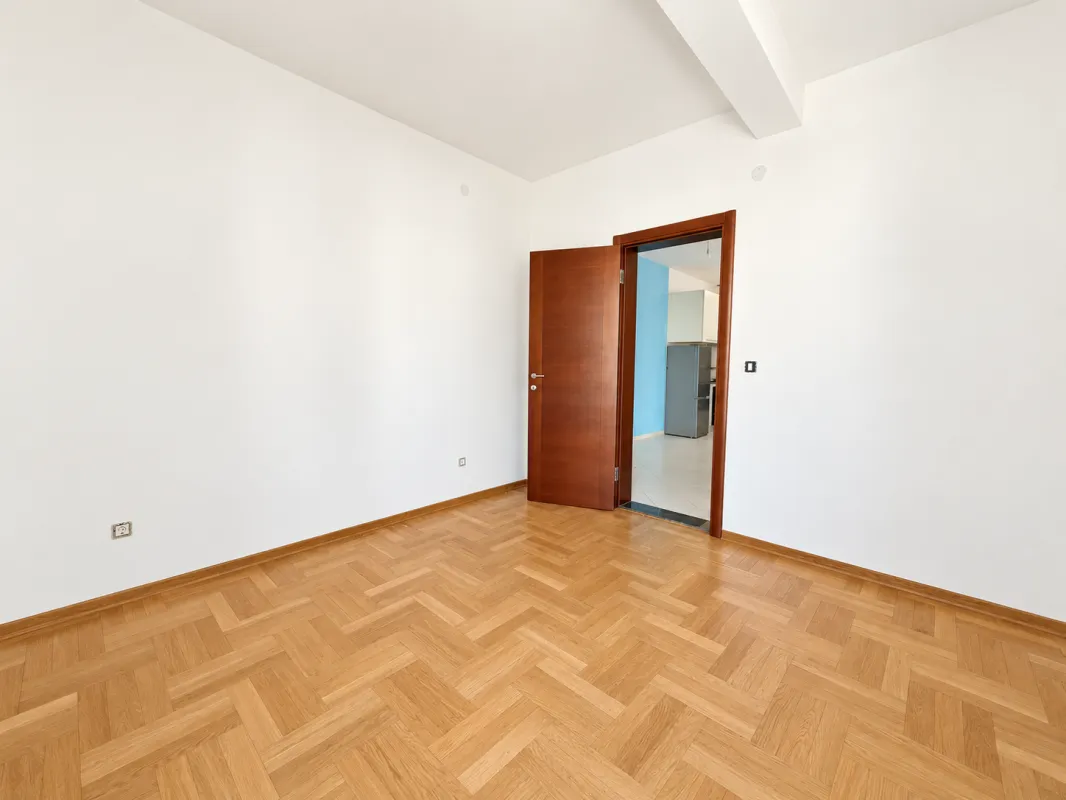 Empty room with white walls and wooden parquet flooring.