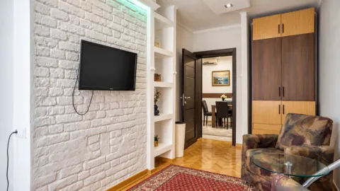 Living room with a white brick wall, television, and armchair. - image 8