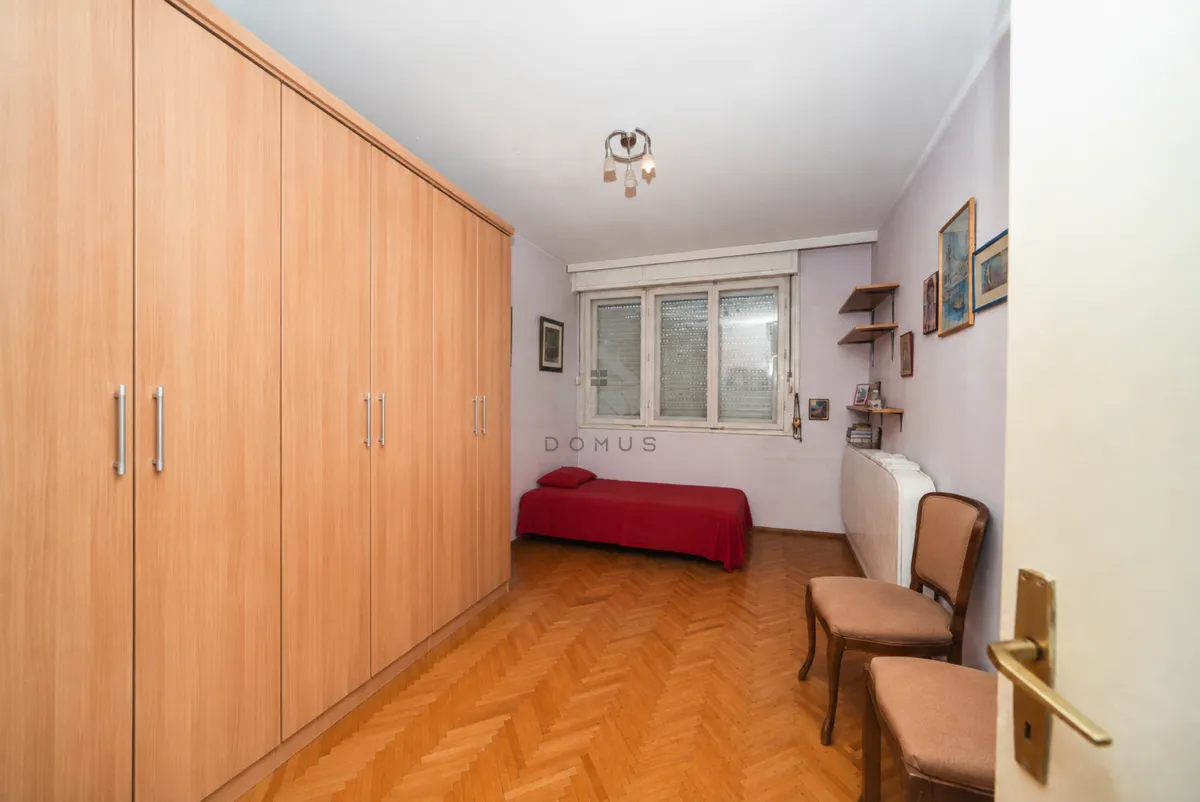 Spavaća soba sa velikim drvenim ormarom, krevetom i dvije stolice.