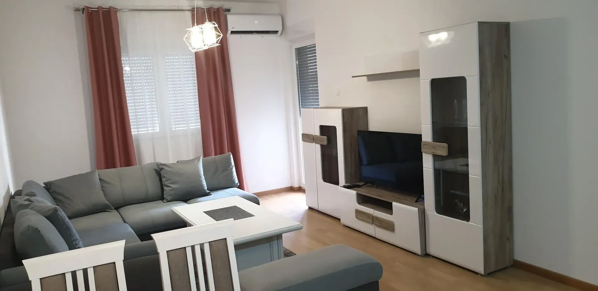 Svijetla dnevna soba sa sivom ugaonom garniturom i modernom TV komodom.