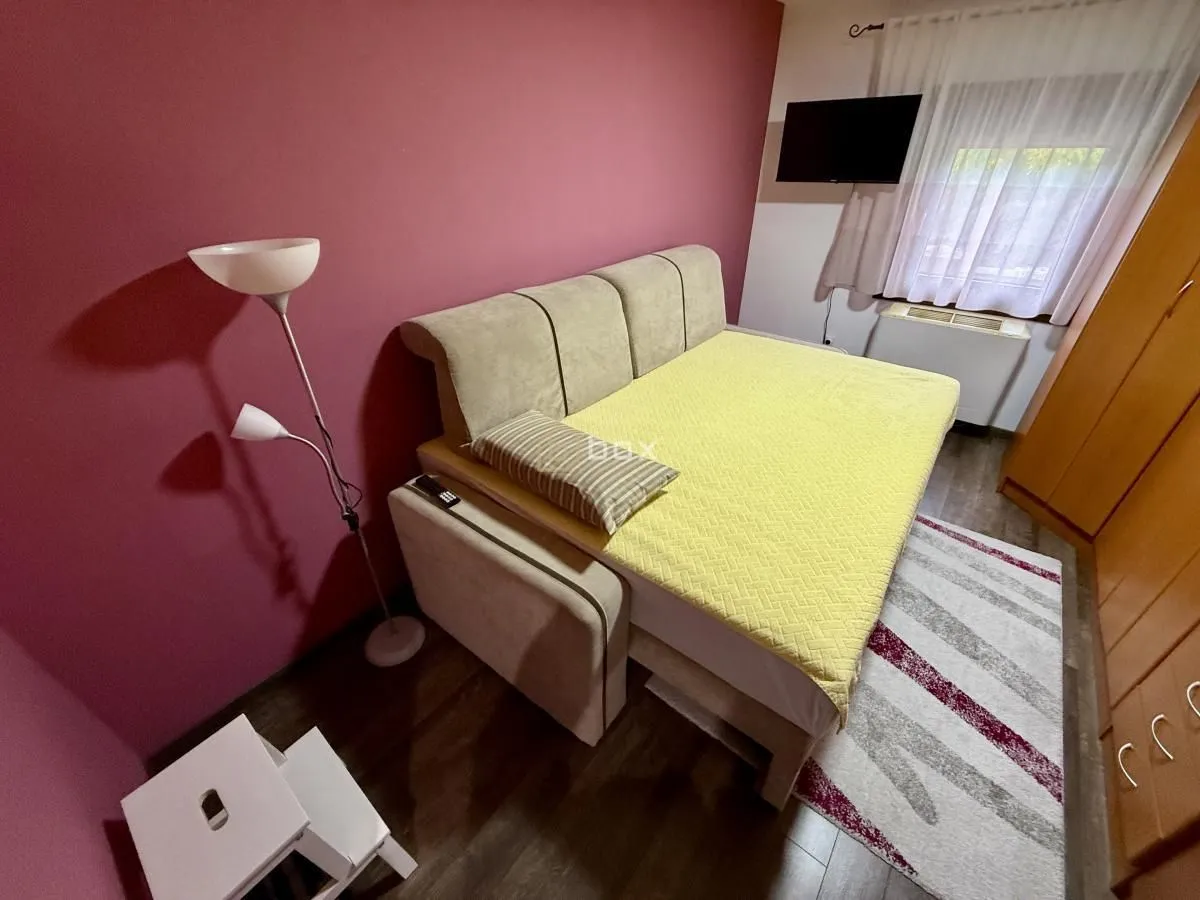 Spavaća soba sa bračnim krevetom, garderoberom i televizorom na zidu.