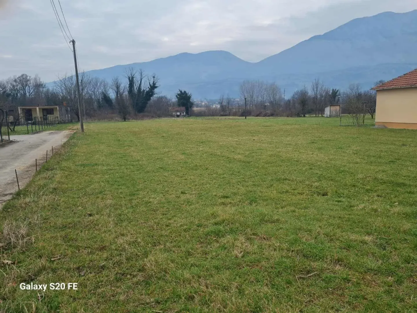 Pogled na prostrano travnato dvorište i okolne planine.