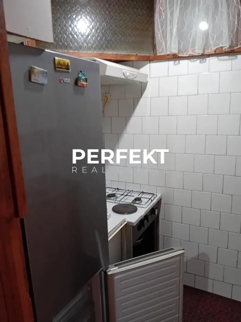 Manja kuhinja sa frižiderom i šporetom obložena belim pločicama.