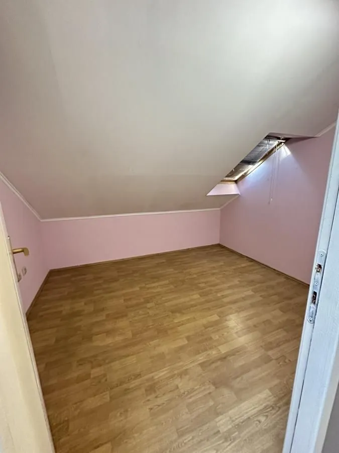 Prazna potkrovna prostorija sa laminatnim podom i roze zidovima.