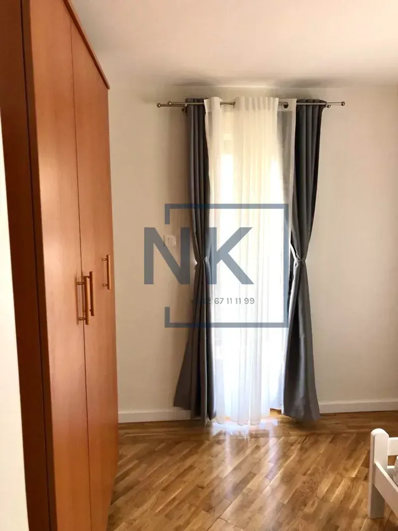 Bedroom with a wooden wardrobe, parquet flooring, and a window with curtains.