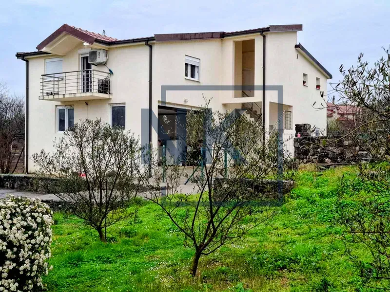 View of the yard and the facade of the house with a balcony and greenery.
