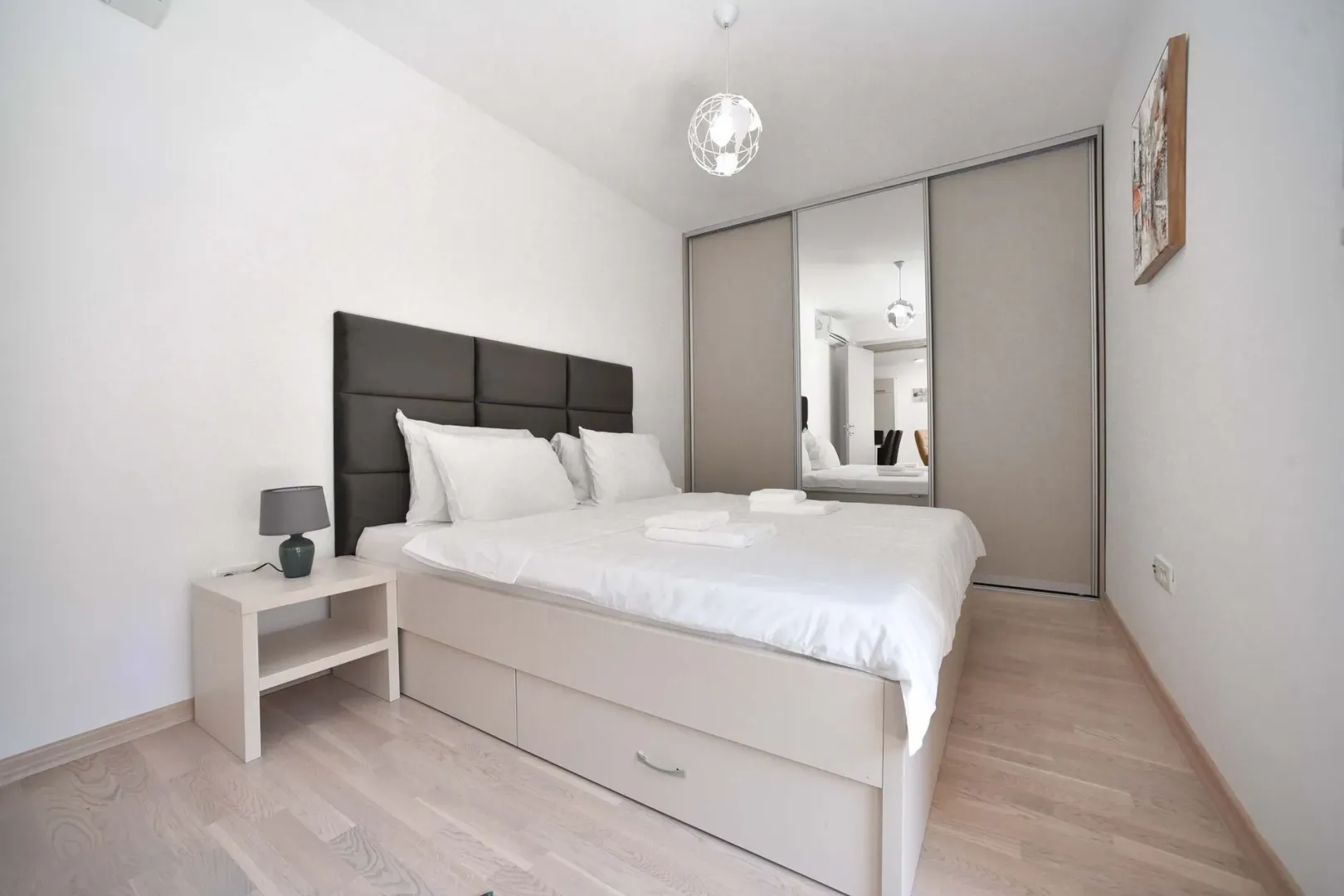Modern bedroom with a double bed, bedside table, and a built-in wardrobe with a mirror.