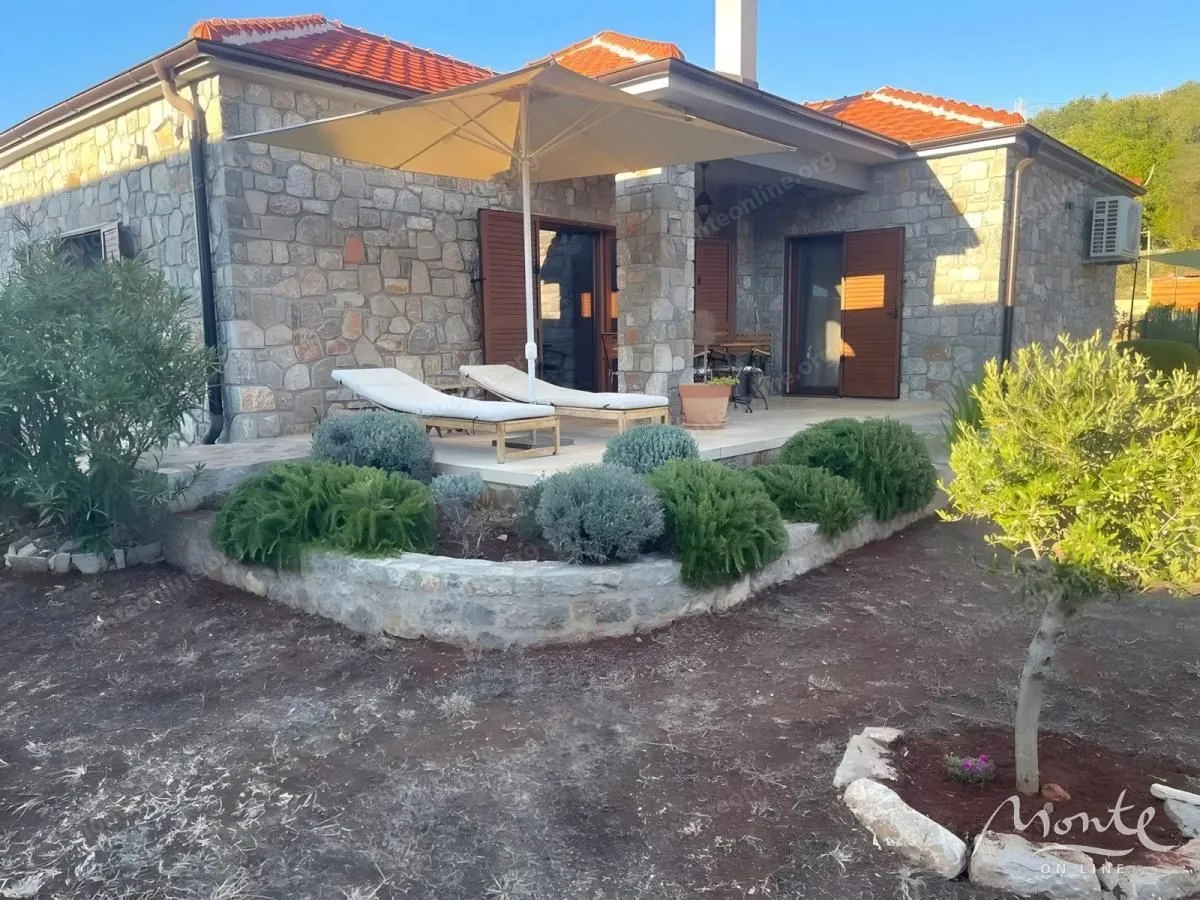 Terasa kamene kuće sa ležaljkama, suncobranom i uređenim dvorištem.
