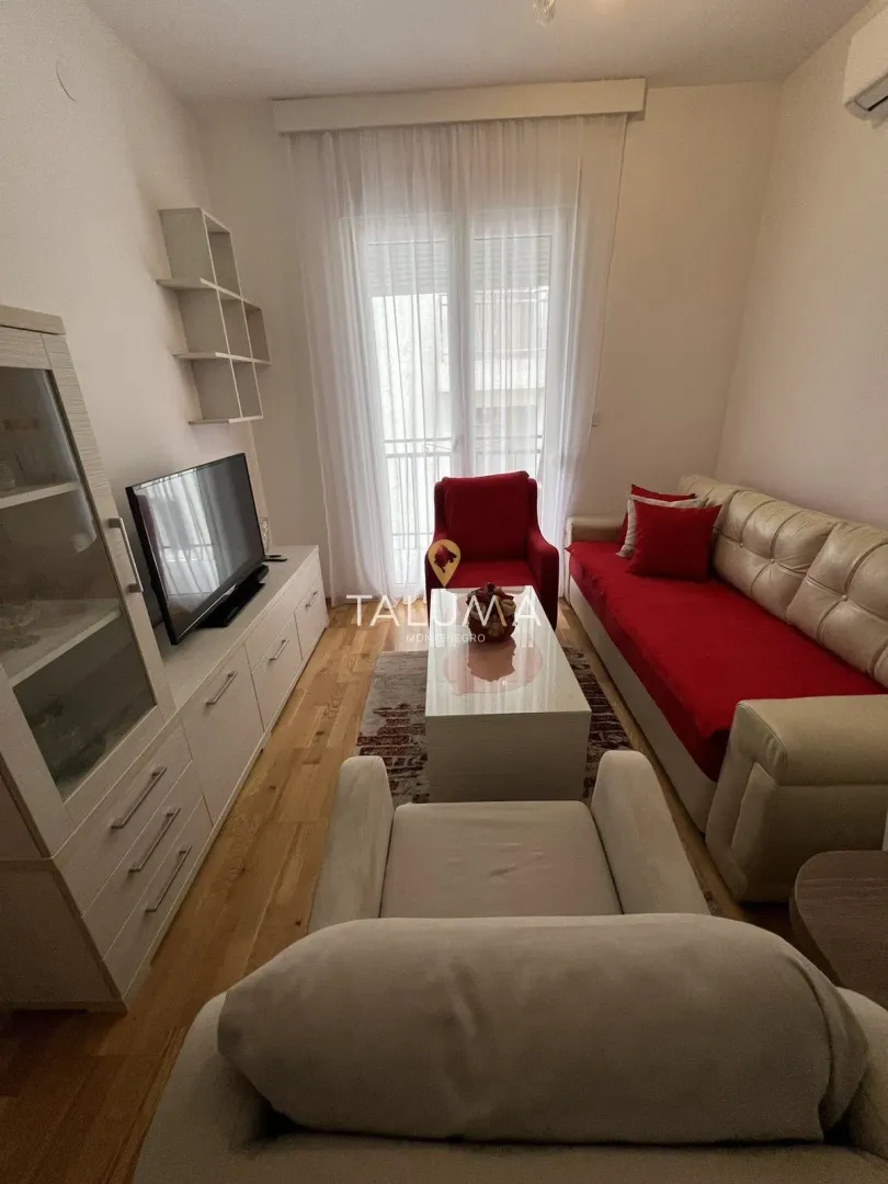 Dnevna soba sa garniturom, televizorom i izlazom na balkon.