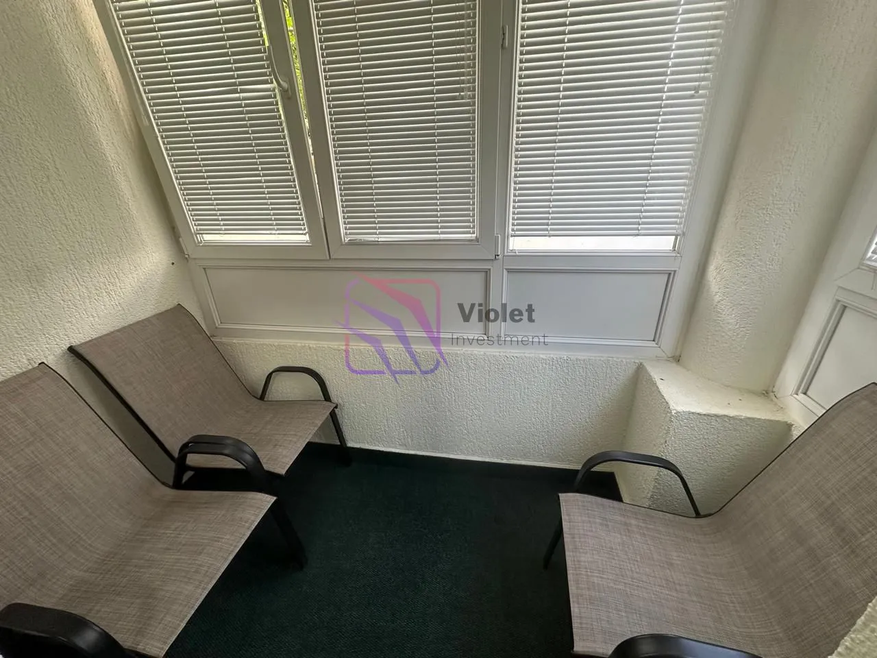 Enclosed balcony with three armchairs and window blinds.