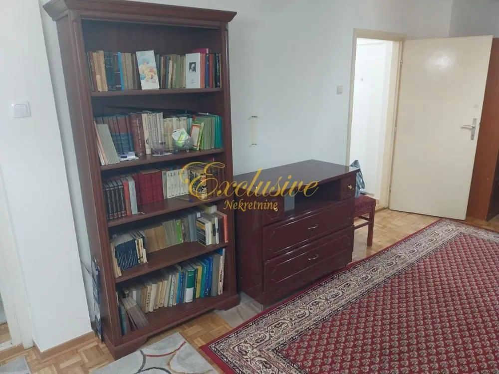 Dnevna soba sa velikom drvenom bibliotekom i komodom.