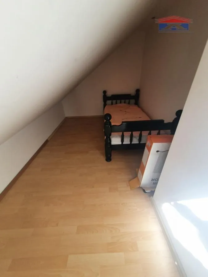 Manja spavaća soba pod kosinom sa krevetom i drvenim podom.