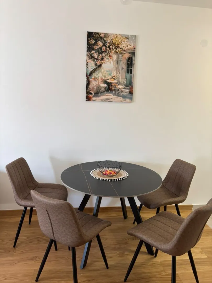 Round dining table with four upholstered chairs and a painting on the wall.