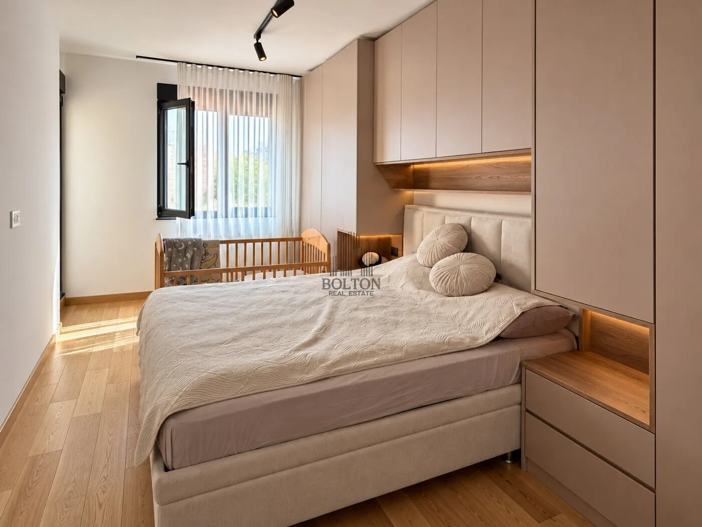 Modern bedroom with a double bed, built-in wardrobes, and a baby cot by the window.