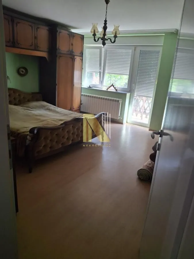 Nameštena spavaća soba sa bračnim krevetom, garderoberom i izlazom na terasu.