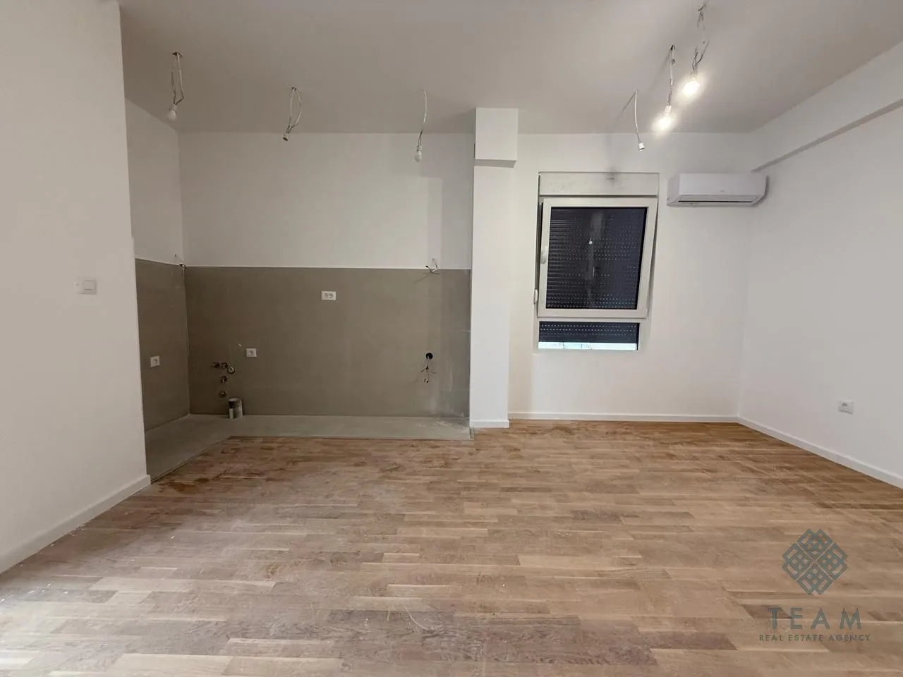 Prazna prostorija sa pripremljenim instalacijama za kuhinju i drvenim podom.