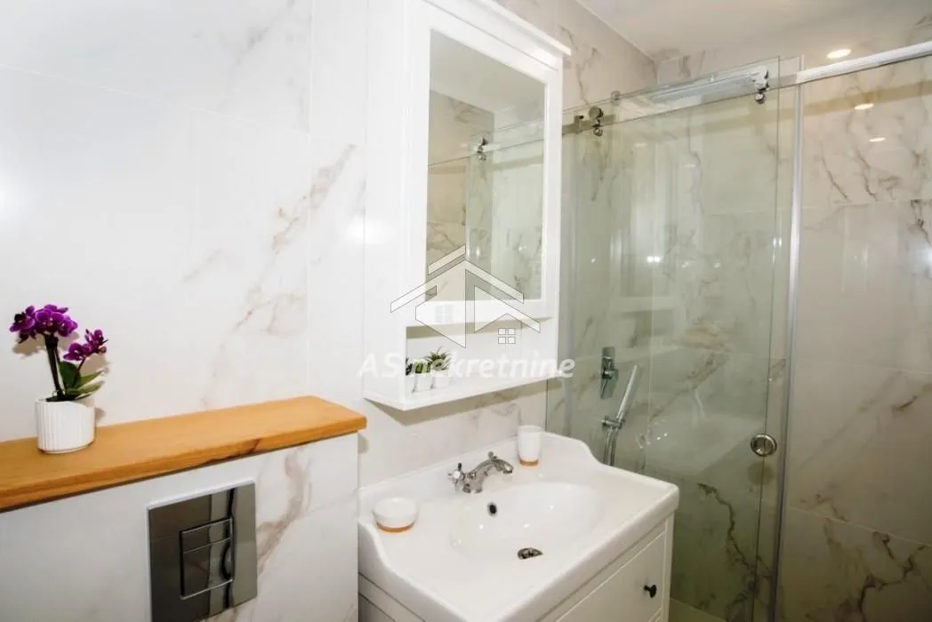 Modern bathroom with a walk-in shower, washbasin, and white marble-effect tiles.