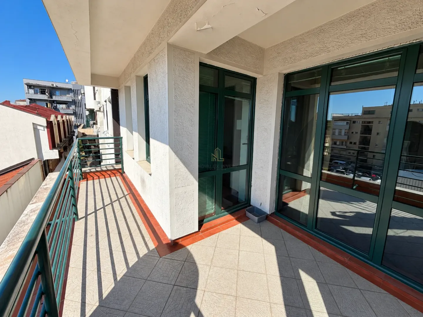 Spacious tiled balcony with a green railing and large glass doors.