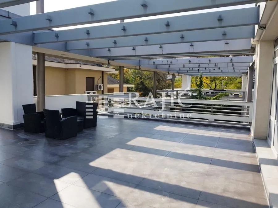 Velika popločana terasa sa pergolom i garniturom za sedenje.