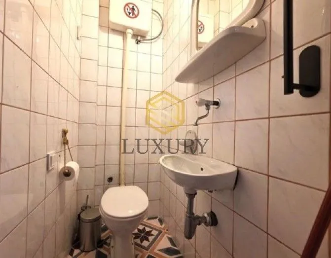 Small bathroom lined with white ceramic tiles featuring a toilet and a sink.