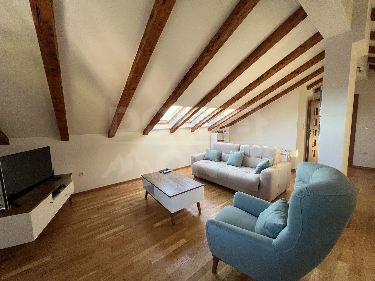 Attic furnished as a living room with wooden ceiling beams and roof windows.