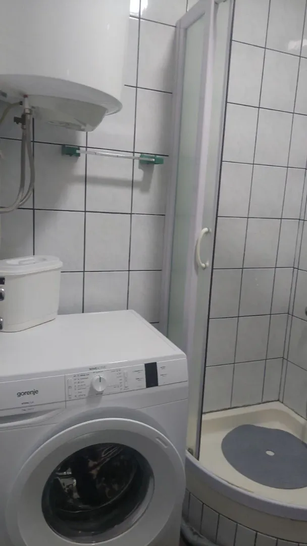 Jednostavno kupatilo sa tuš kabinom, bojlerom i veš mašinom.