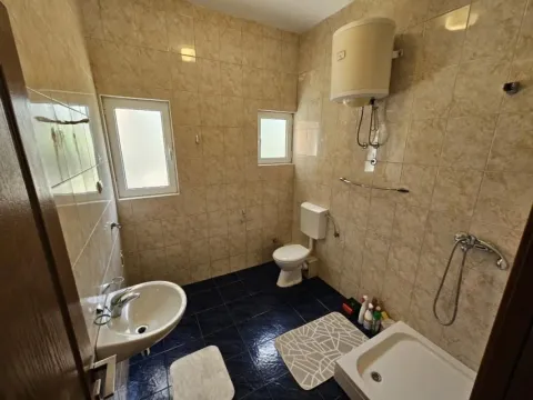 Kupatilo obloženo keramičkim pločicama sa toaletom, umivaonikom i tuš kabinom. - image 5