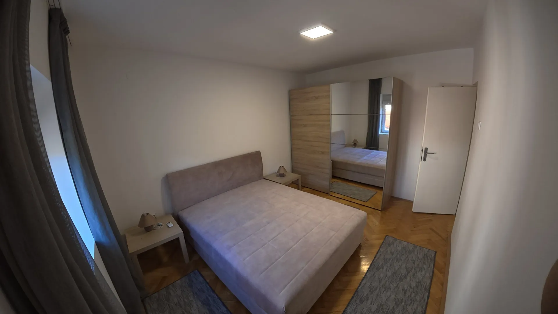 Furnished bedroom with a double bed, mirrored wardrobe, and parquet flooring.