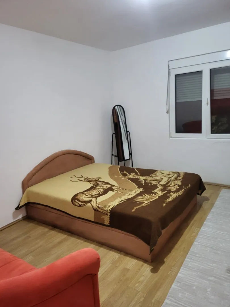 Jednostavno namještena spavaća soba sa bračnim krevetom i ogledalom.