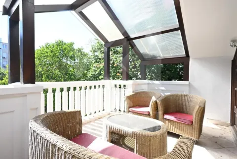Covered terrace with wicker furniture and a view of greenery. - image 22