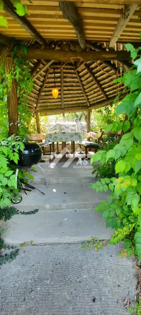 Natkrivena drvena senica sa stolom za sedenje i roštiljem u dvorištu.