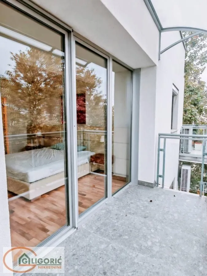 Balcony with glass railing and view through a large window opening into the interior of the room.