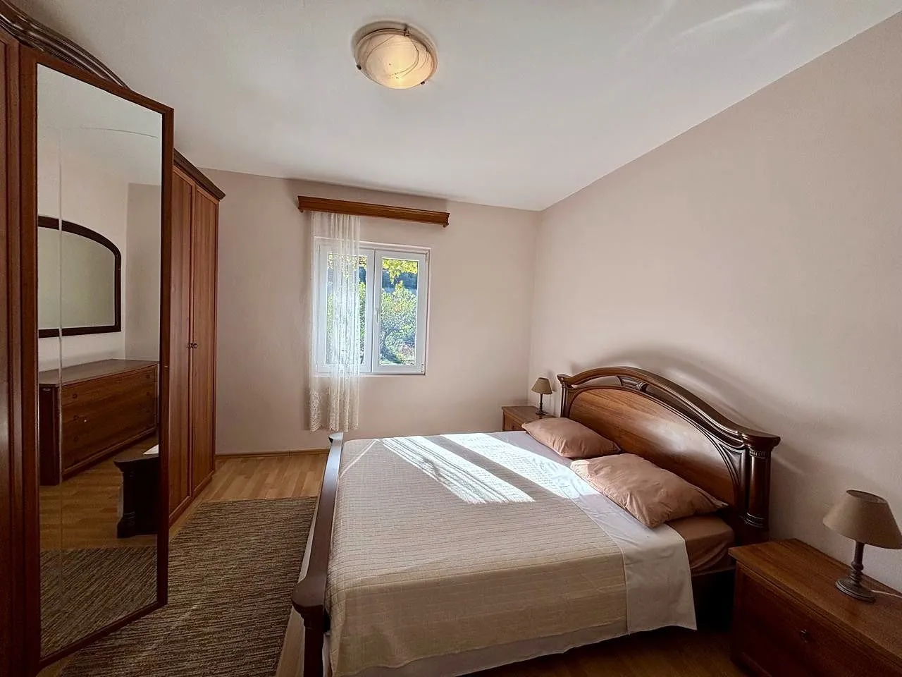 Spacious bedroom with a double bed, wooden wardrobe with a mirror, and nightstands.