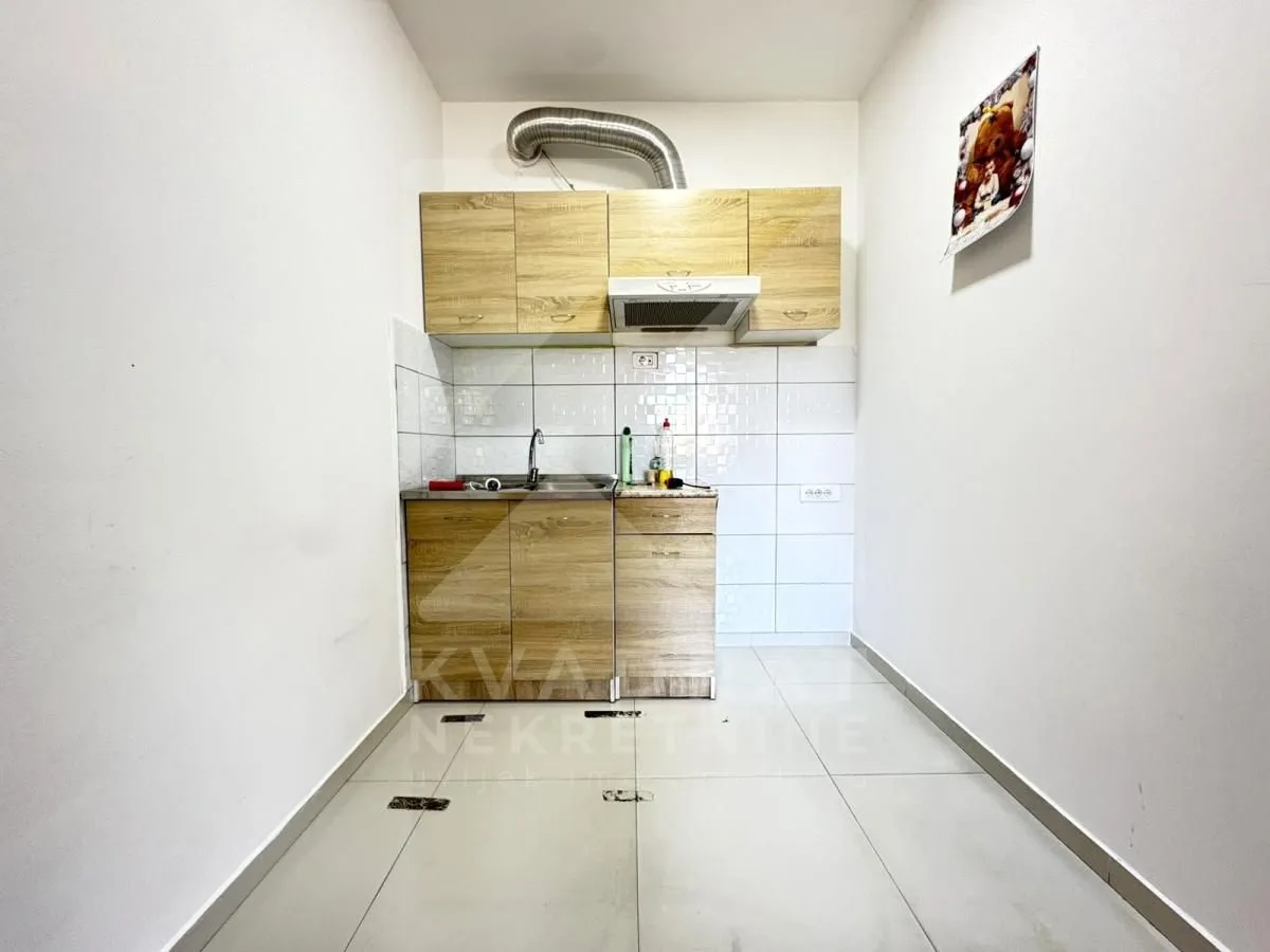 Small kitchen with wooden cabinetry and white wall tiles.