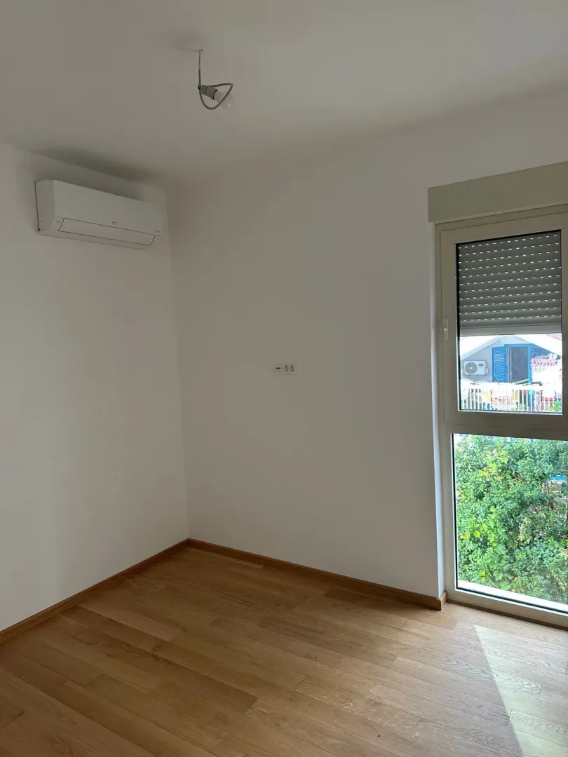 Empty room with hardwood floors, an air conditioner, and a window.