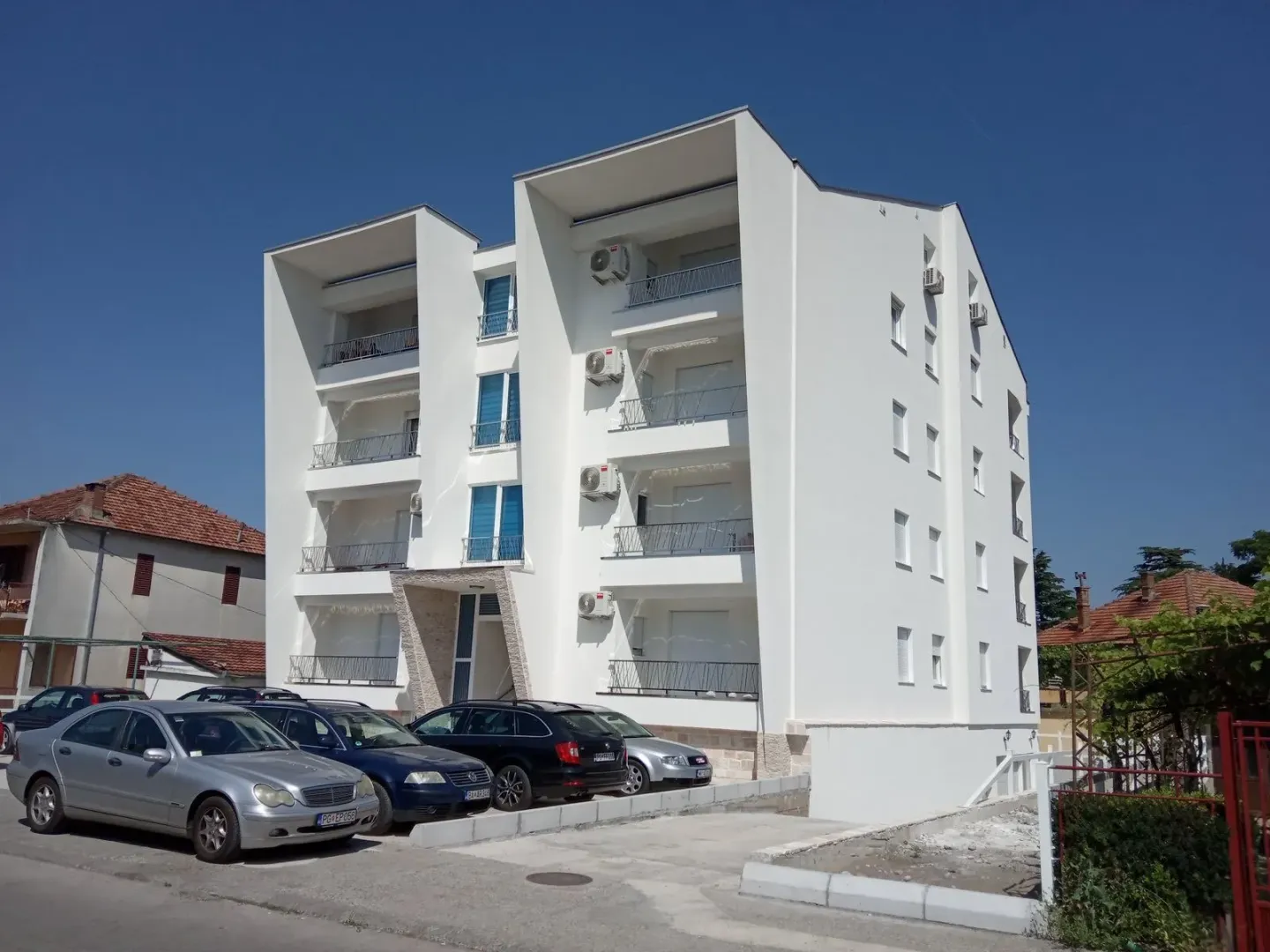 Spoljašnji izgled moderne stambene zgrade sa parkingom ispred.