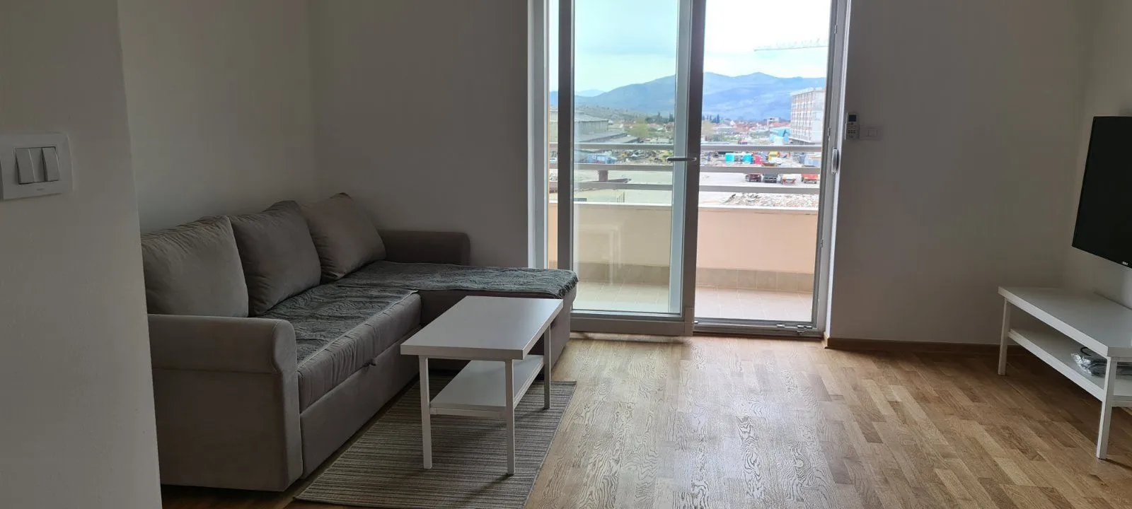 Svijetla dnevna soba sa sivom ugaonom garniturom i izlazom na balkon.